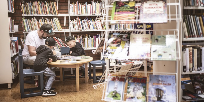 Pappa och två barn läser i biblioteket